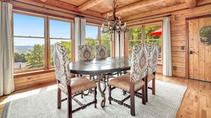 A wooden dining room with a round table and patterned chairs, large windows with curtains, and a chandelier. - Sequoyah Lodge - 1.5 mi to DT (Fayetteville)