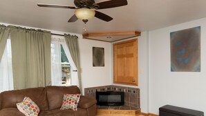 A living room with a brown leather sofa, a ceiling fan, a fireplace, and a painting on the wall.