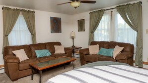 A room with two brown leather sofas, a small wooden coffee table, a single lamp, and a large bed with striped bedding.