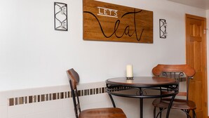 A dining area with a round table, two chairs, and a wooden wall decoration with the text "LET'S eat".