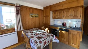 A compact kitchen with wooden cabinets, a dining table with a patterned tablecloth, and a window with curtains. - 150m from ski slopes, 1st floor, view ski slopes, balcony, tv, 34m², Les Saisies (Les Saisies)