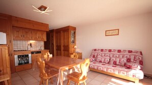 A kitchen with wooden cabinets, a dining table with chairs, and a sofa with a patterned cover. - 150m from ski slopes, 1st floor, view ski slopes, balcony, tv, 34m², Les Saisies (Les Saisies)