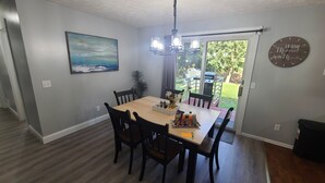 Un espace repas comprenant une table, des chaises, un lustre, un tableau et une vue sur l’extérieur.