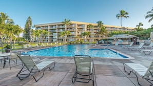 A hotel pool area with lounge chairs, a swimming pool, palm trees, and a multi-story building in the background. - Steps to the ocean sunny Kihei, Maui Sunset A104 (Kihei)