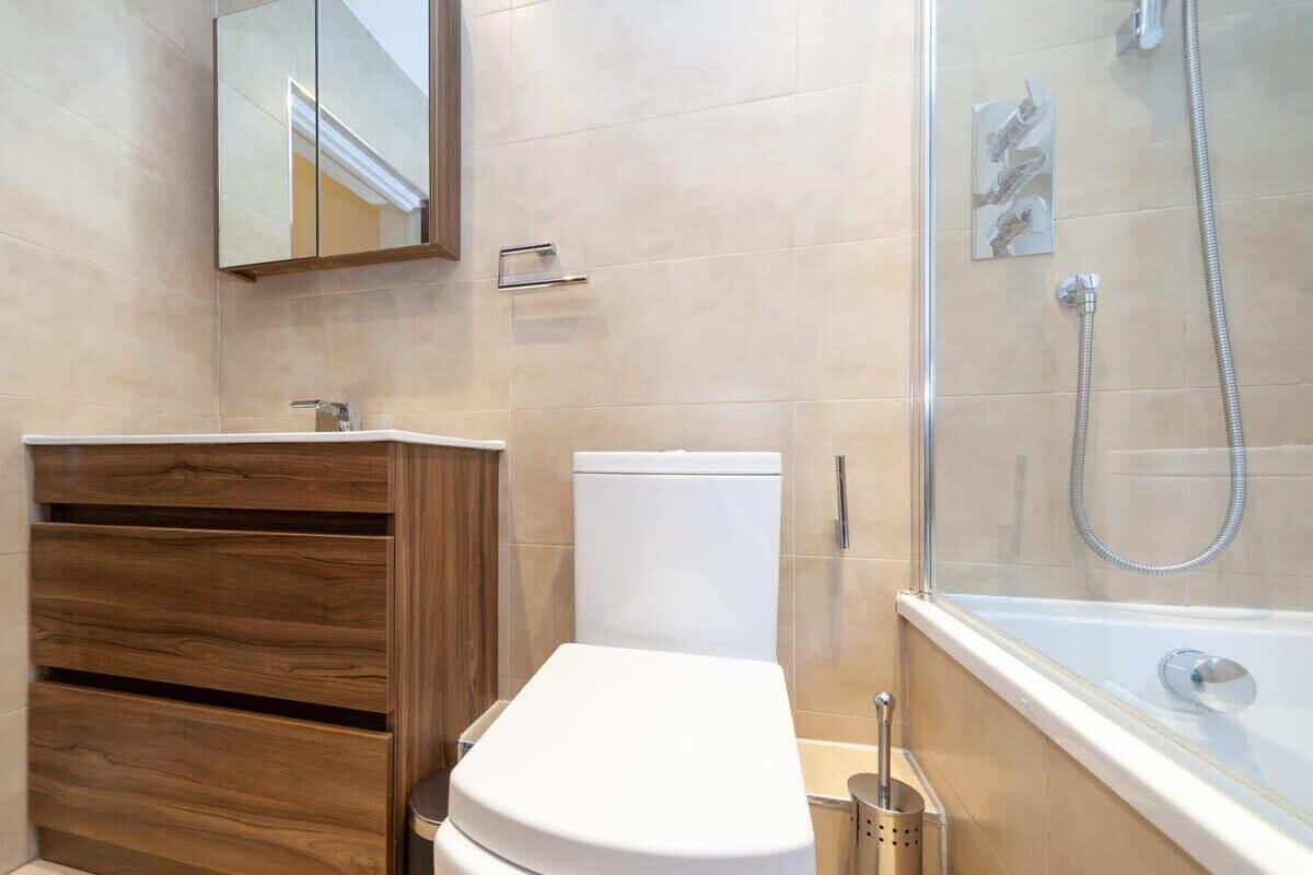 A bathroom with a wooden vanity, a white toilet, a glass shower enclosure, and a bathtub.