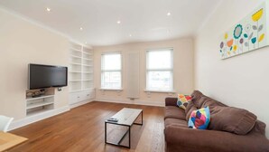 Ein modernes Wohnzimmer mit Flachbildfernseher, braunem Sofa, Couchtisch und einem farbenfrohen Kunstwerk an der Wand.