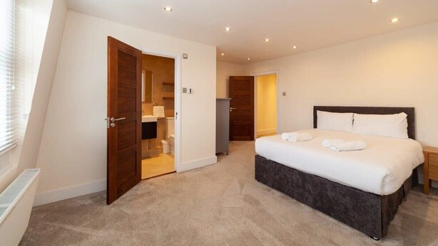 Ein Schlafzimmer mit einem großen Bett, einer Holztür zu einem Badezimmer und einem kleinen Nachttisch.