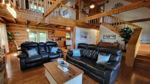 A spacious living area with a wooden staircase, black leather sofas, a wooden coffee table, and a kitchen in the background. - 20% OFF Lake View Retreat- Lake & Mountain View, Hot Tub, Fire Pit, Porch Swing (Dandridge)