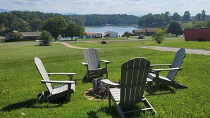 A grassy outdoor area with Adirondack chairs and a view of a lake and buildings in the distance. - 20% OFF Lake View Retreat- Lake & Mountain View, Hot Tub, Fire Pit, Porch Swing (Dandridge)