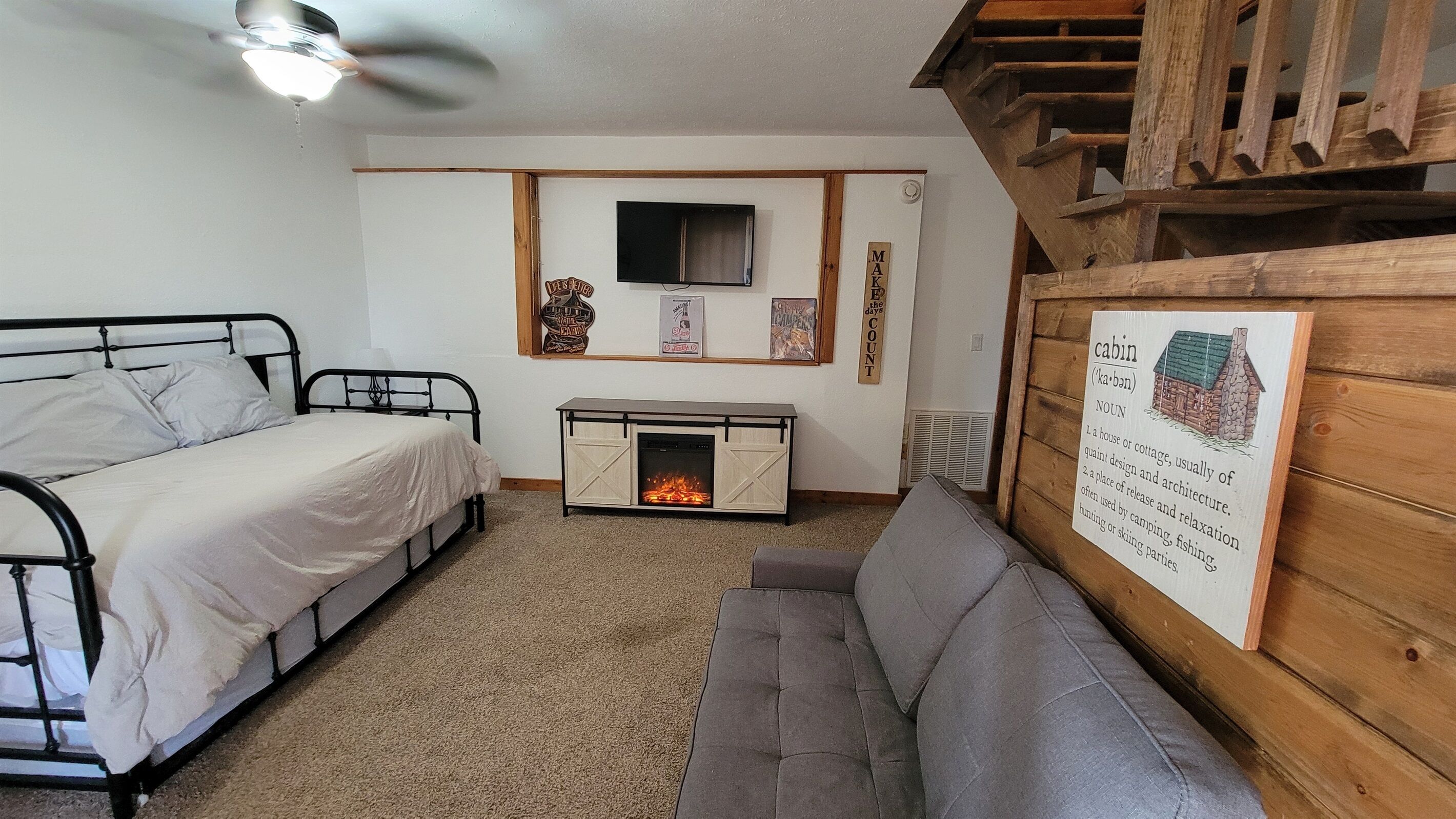 Ein gemütliches Blockhauszimmer mit Bett, Sofa, Kamin und Wandfernseher.