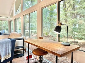 A room with large windows, a wooden desk, a chair, and a lamp.