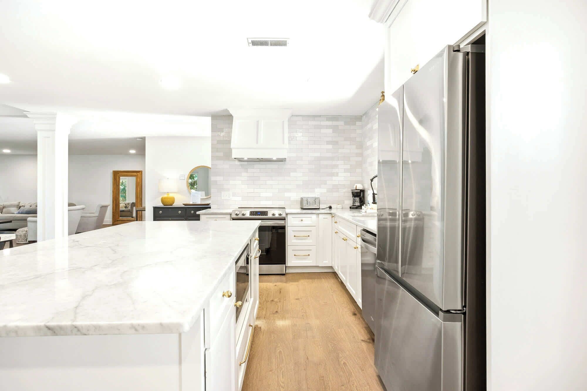 A modern kitchen with white cabinets, a marble countertop, stainless steel appliances, and a wooden floor.