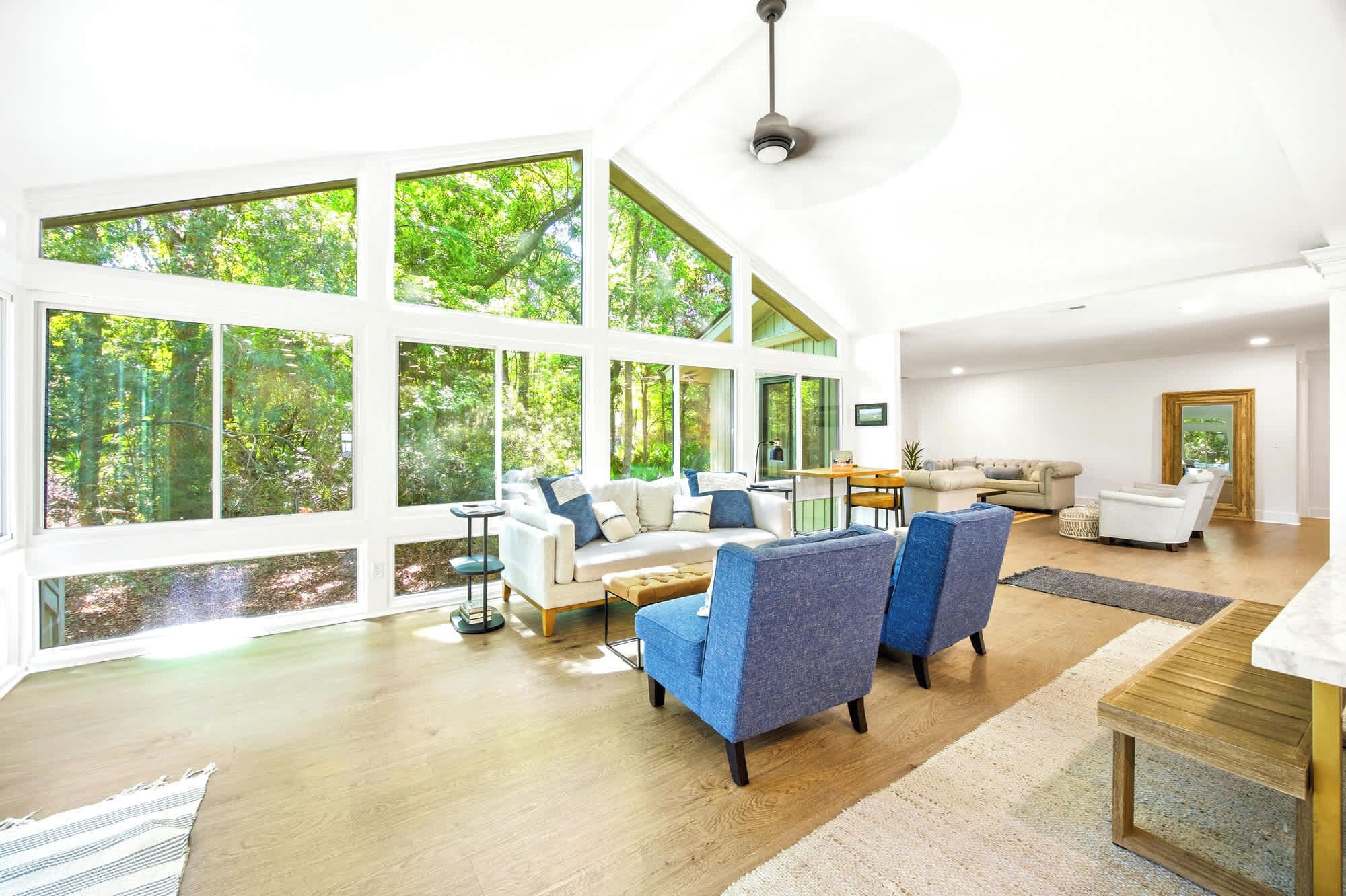 A spacious living room with large windows, a ceiling fan, and a wooden floor.
