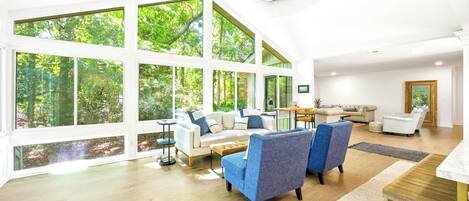 A spacious living room with large windows, a ceiling fan, and a wooden floor.