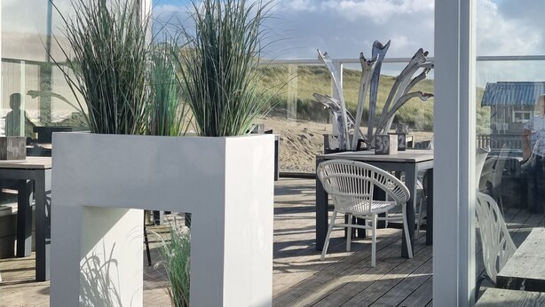 Een terras buiten met een modern ontwerp, met een witte plantenbak met hoge grassen, een witte stoel en een tafel.