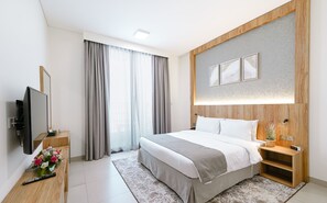 A modern hotel room with a large bed, a flat-screen TV, a bedside table with a vase of flowers, and a wooden nightstand. - Azur Regency Hotel Apartment (Dubai)