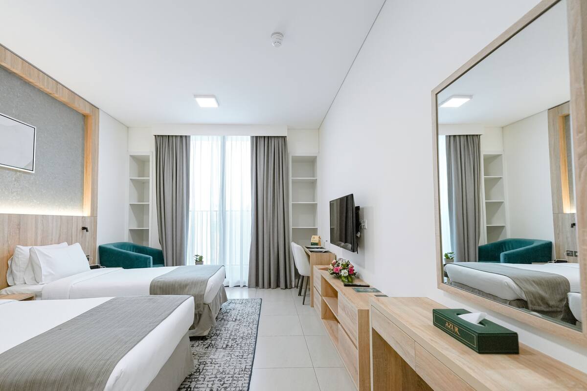 A modern hotel room with two beds, a desk, a mirror, and a TV.