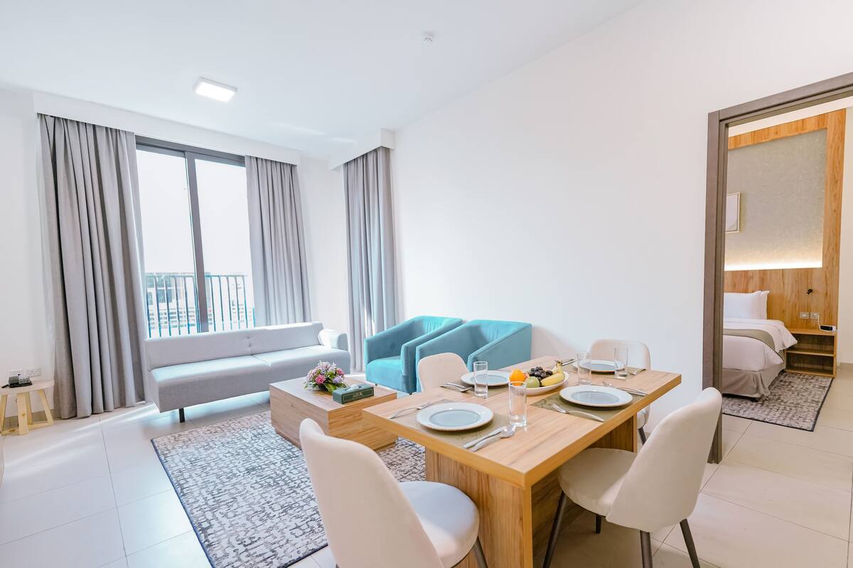 A modern hotel room with a dining area, a sofa, and a balcony with curtains.