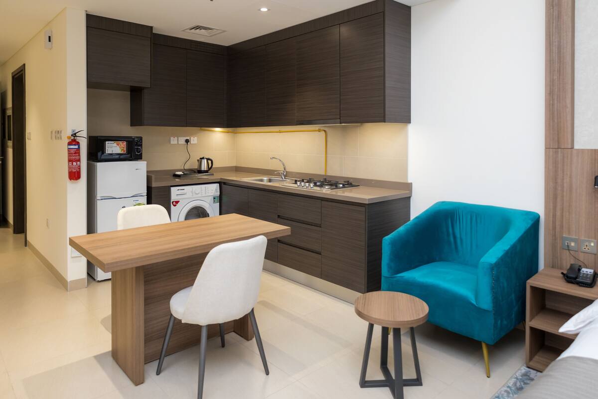 A compact kitchen with modern appliances, a dining area with a table and chairs, and a small stool.