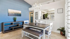 A modern dining area with a wooden table and white chairs, a bench, a chandelier, and a blue accent wall.