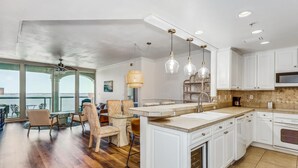 Une cuisine spacieuse avec des meubles blancs, un grand îlot central et une vue sur l’extérieur.
