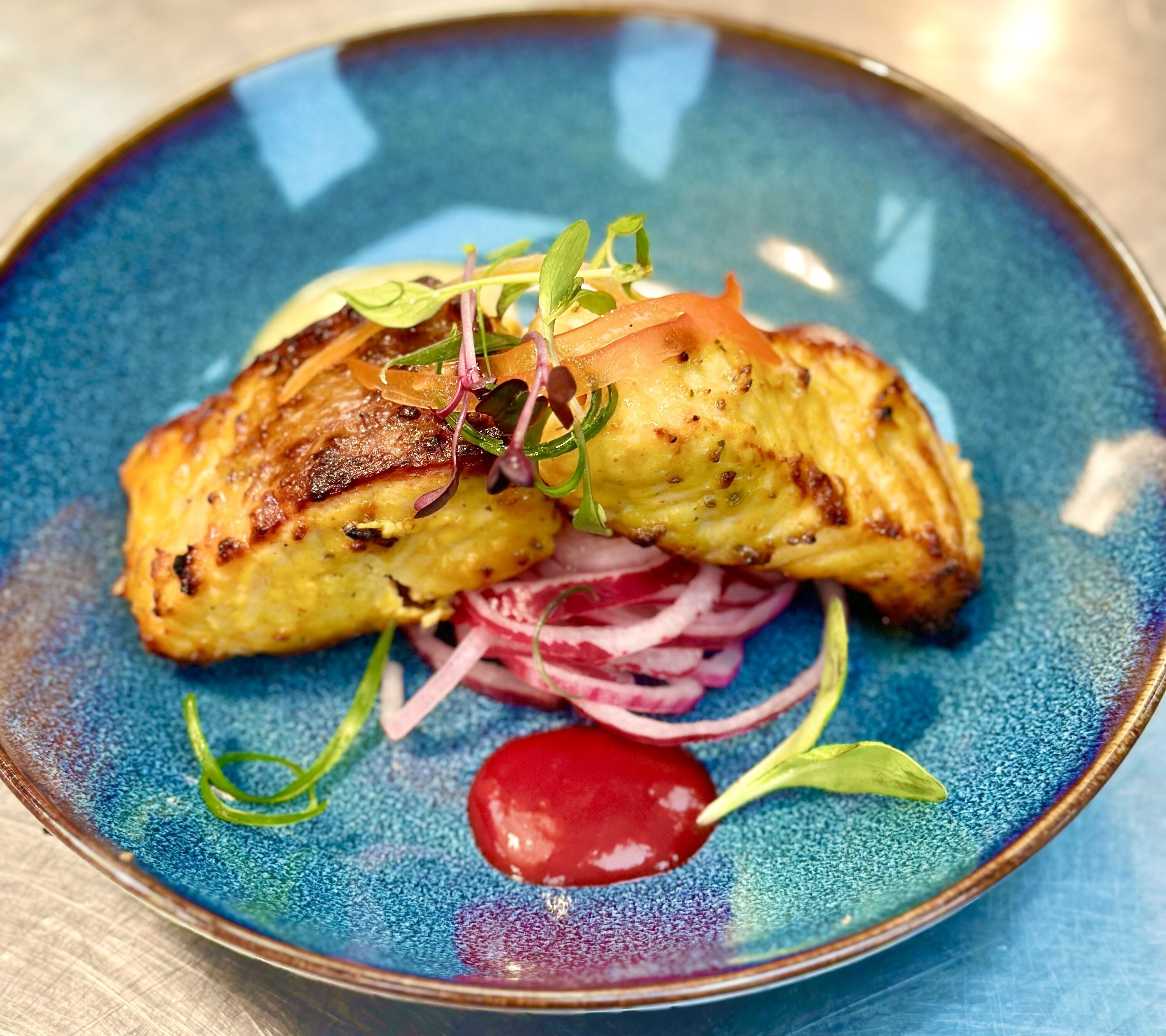 A plate with grilled fish, red onion rings, and a cherry.