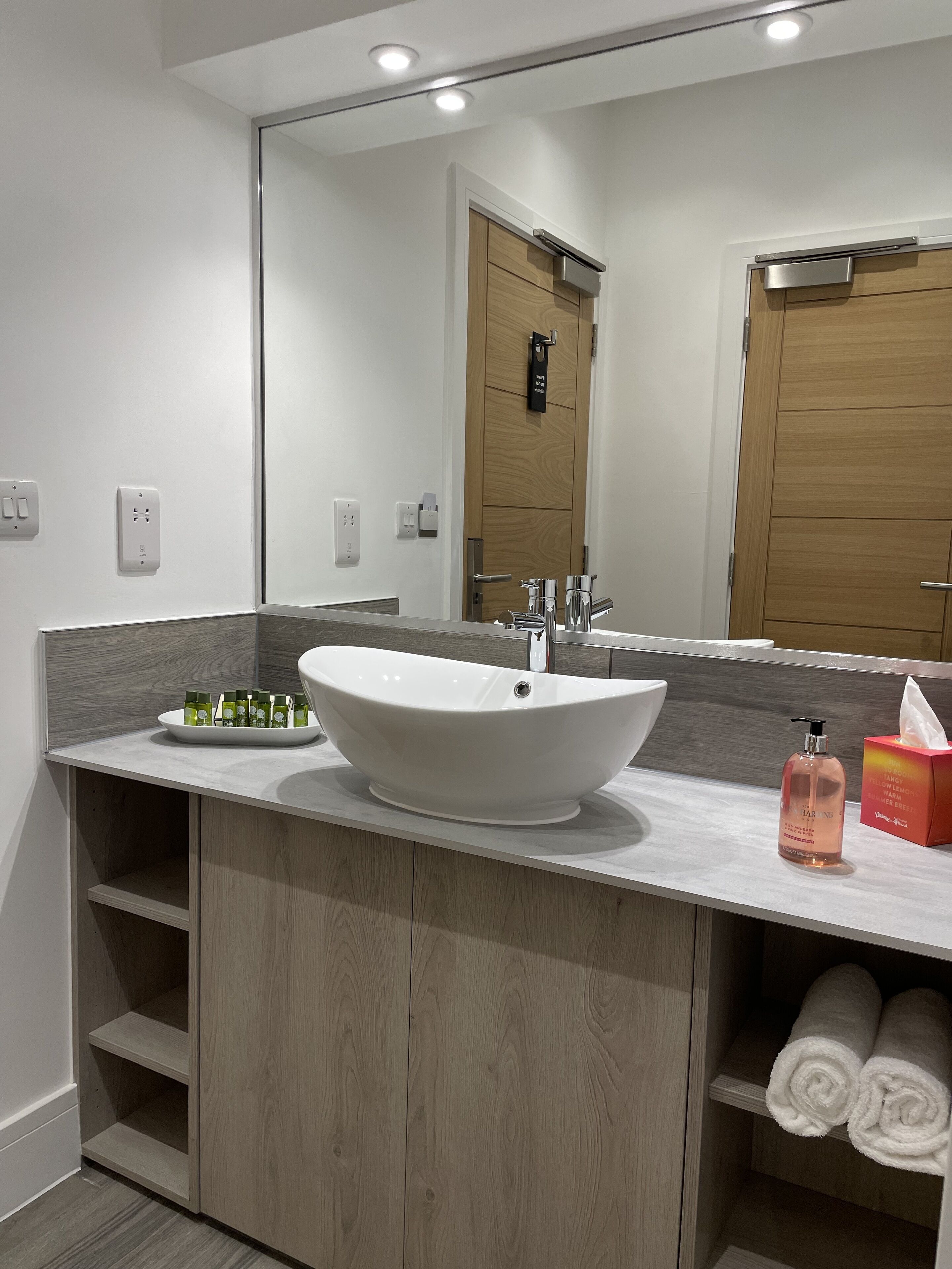 Un baño moderno con un lavamanos de diseño, un espejo y un mueble de tocador de madera.
