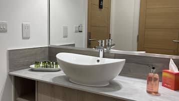Un baño moderno con un lavamanos de diseño, un espejo y un mueble de tocador de madera.