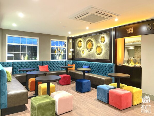 A modern lounge area with a blue sofa, colorful ottomans, and a wall-mounted art piece.