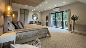A modern bedroom with a large bed, a sofa, a mirror, and a view of the outdoors through a sliding glass door. - The Boutique Hotel by The Snooty Mehmaan (Faringdon)