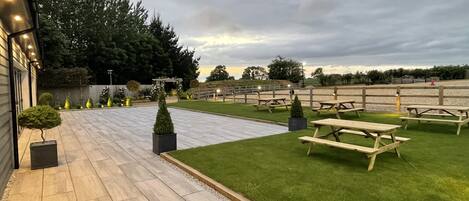 A well-maintained outdoor area with a paved walkway, picnic tables, and neatly trimmed grass.