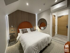 A modern hotel room with a large bed, a round mirror, a small table, and a wooden door.