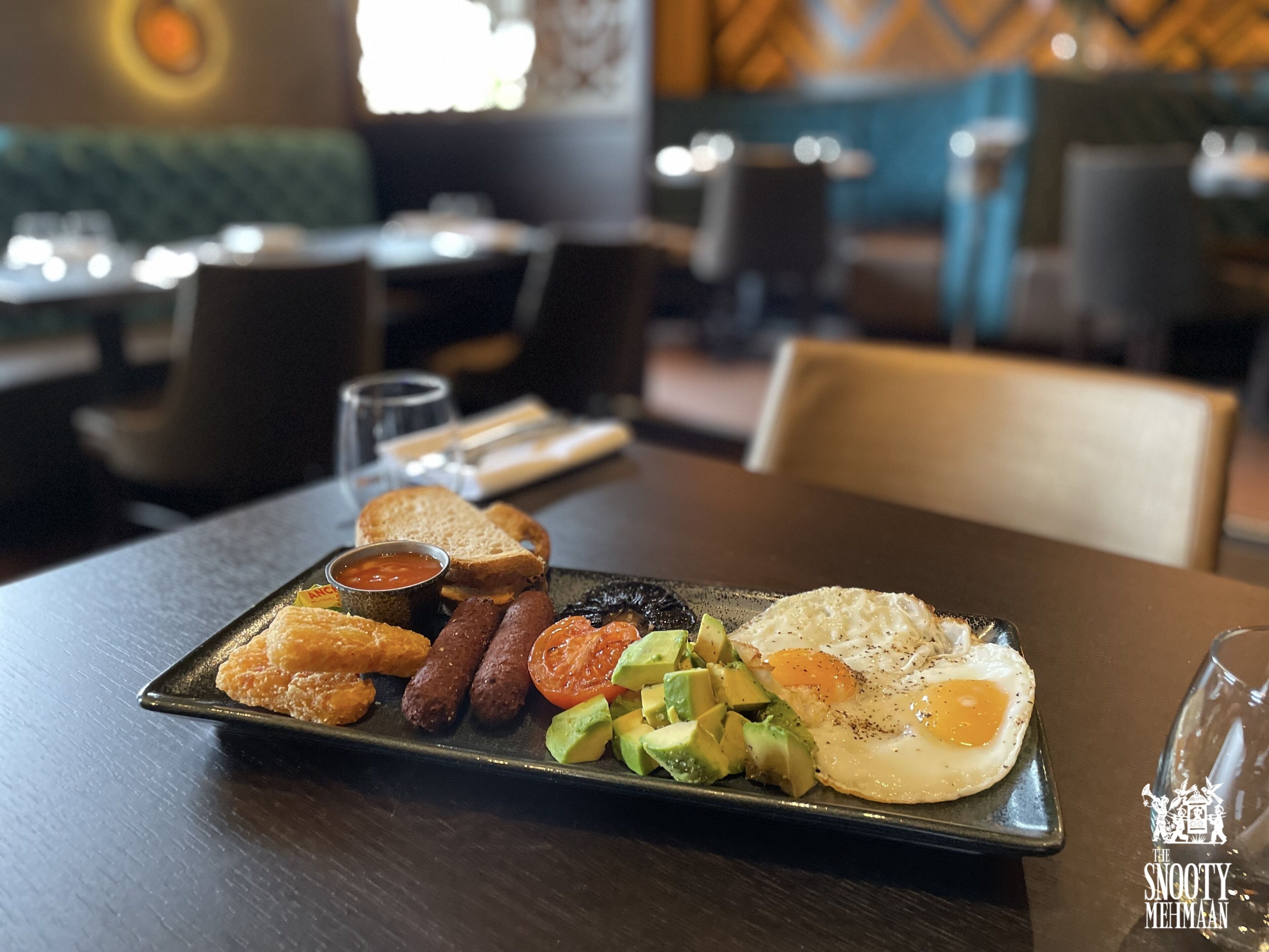 Un plat d'esmorzar amb ous, botifarra, alvocat i torrades sobre un plat fosc.