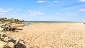 Une vaste plage de sable fin, un ciel bleu dégagé, quelques nuages épars et une mer calme.