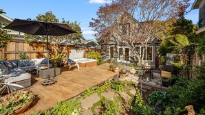 Un jardin avec une terrasse en bois, du mobilier d’extérieur, un barbecue et une variété de plantes.