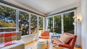 Un salon moderne avec de grandes fenêtres, un canapé, un fauteuil, une petite table et une lampe.