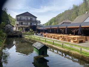 Un restaurante a la orilla del río con terraza, una casa de madera y un edificio grande con balcón.