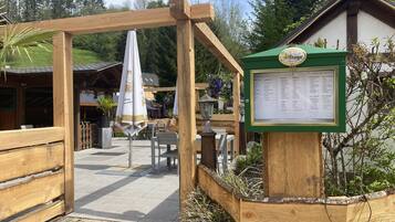 An outdoor seating area with wooden tables and chairs, a menu board, and a wooden pergola structure.