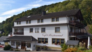 A two-story building with a cafe and restaurant sign, featuring a balcony on the upper floor and a small outdoor seating area. - Theis-Mühle (Biersdorf am See)