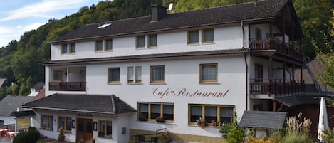 A two-story building with a cafe and restaurant sign, featuring a balcony on the upper floor and a small outdoor seating area.