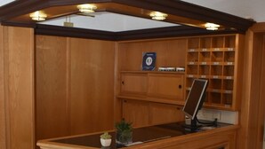A reception desk with a wooden finish, a computer monitor, and a small potted plant. There is a sign above the desk and a shelf with numbered compartments. - Theis-Mühle (Biersdorf am See)