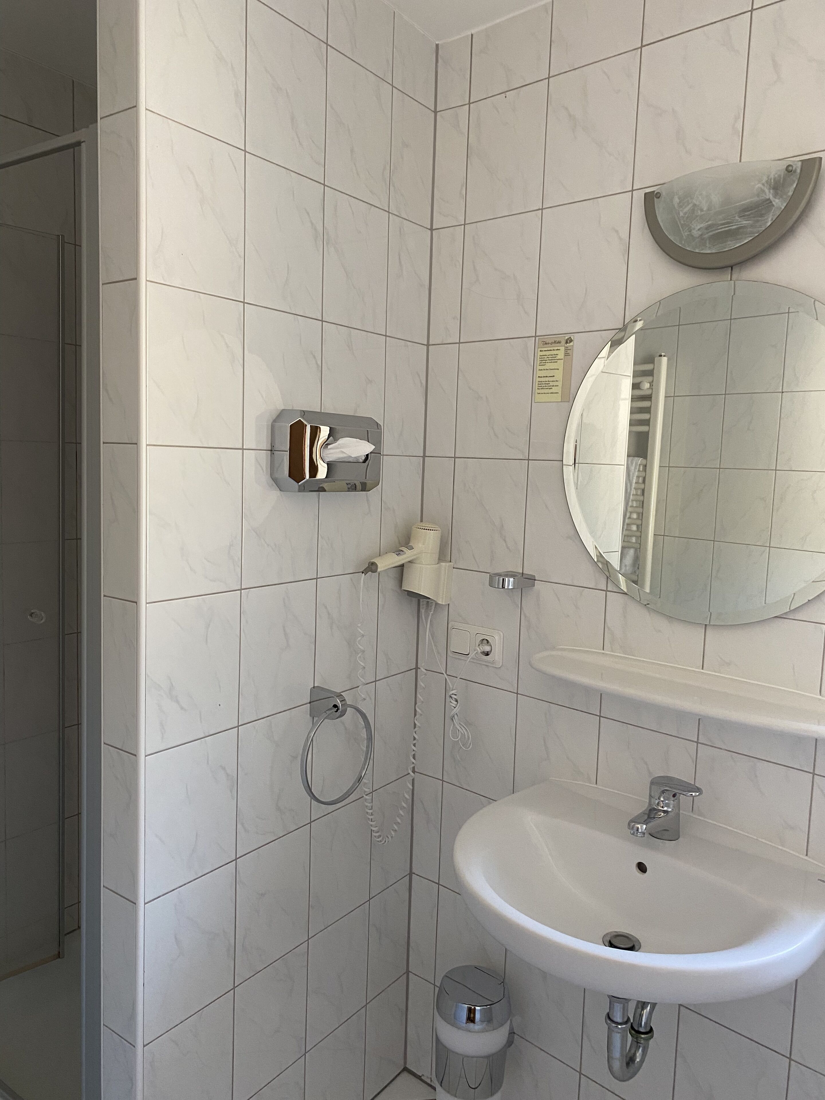 Ein Badezimmer mit weißen Marmorfliesen, einem Waschbecken, einem Spiegel, einem Handtuchhalter und einer Toilette.