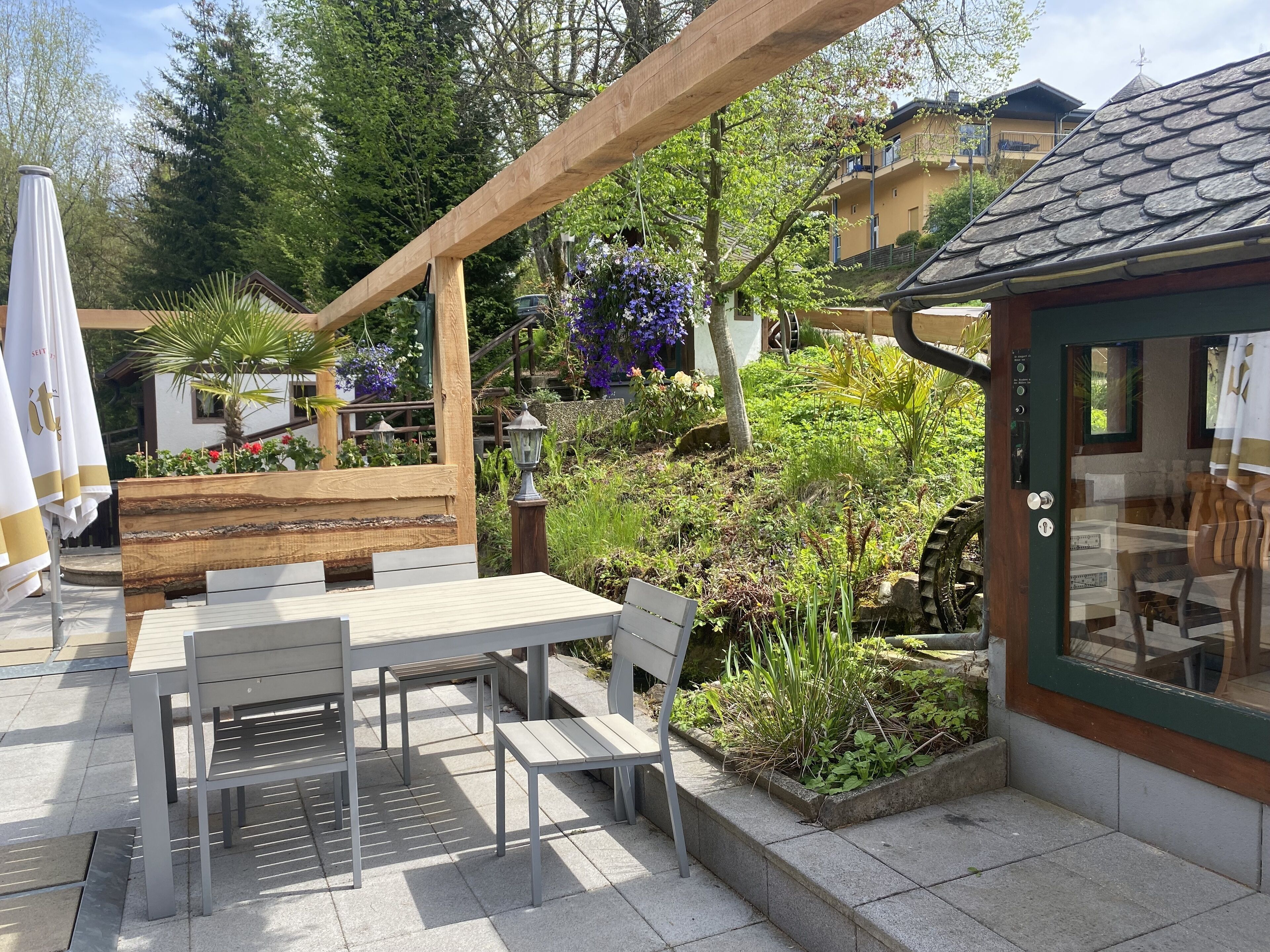 A patio with outdoor seating, a wooden pergola, and a garden with various plants and flowers.