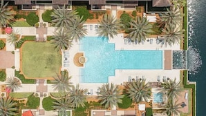 Vista aérea de un resort con varias edificaciones, una piscina central y palmeras.