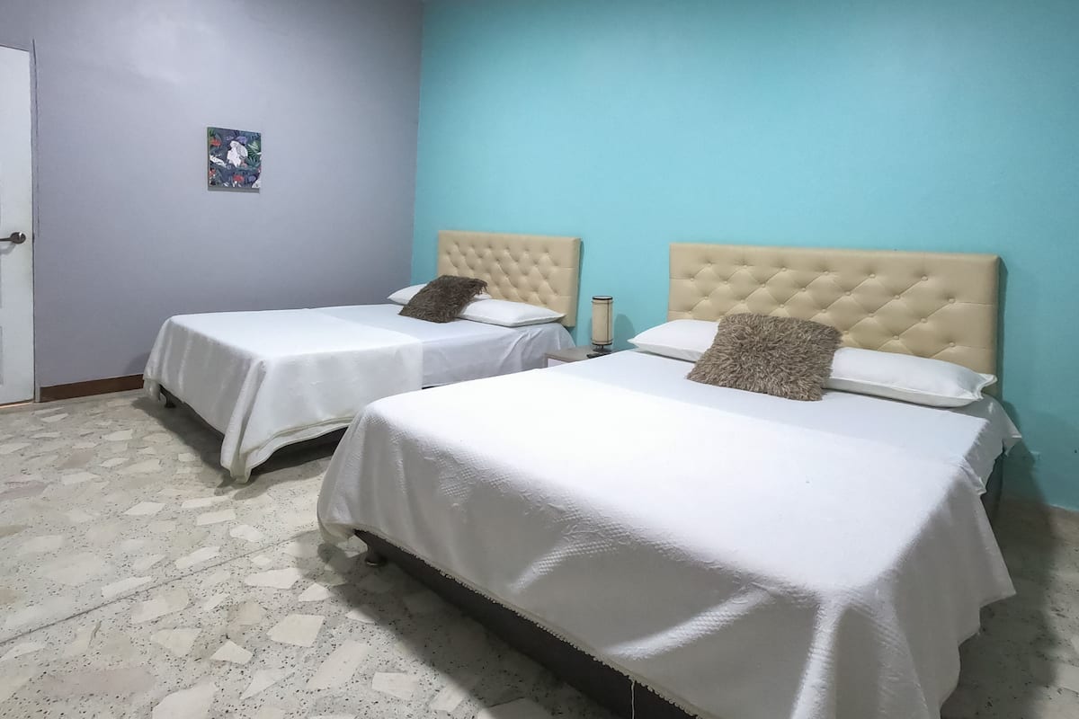 A hotel room with two beds, each with a tufted headboard, white bedding, and a small bedside table with a lamp.
