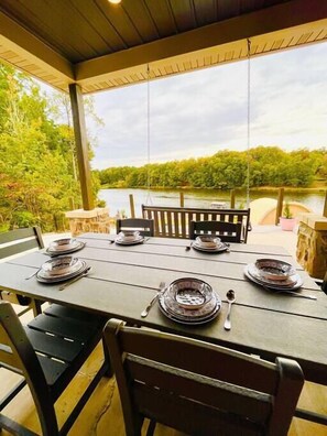 An outdoor dining area with a table set for four, overlooking a lake and surrounded by greenery.