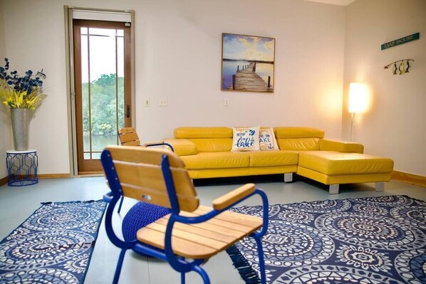 A room with a yellow sofa, a blue chair, a patterned rug, a painting, and a lamp.