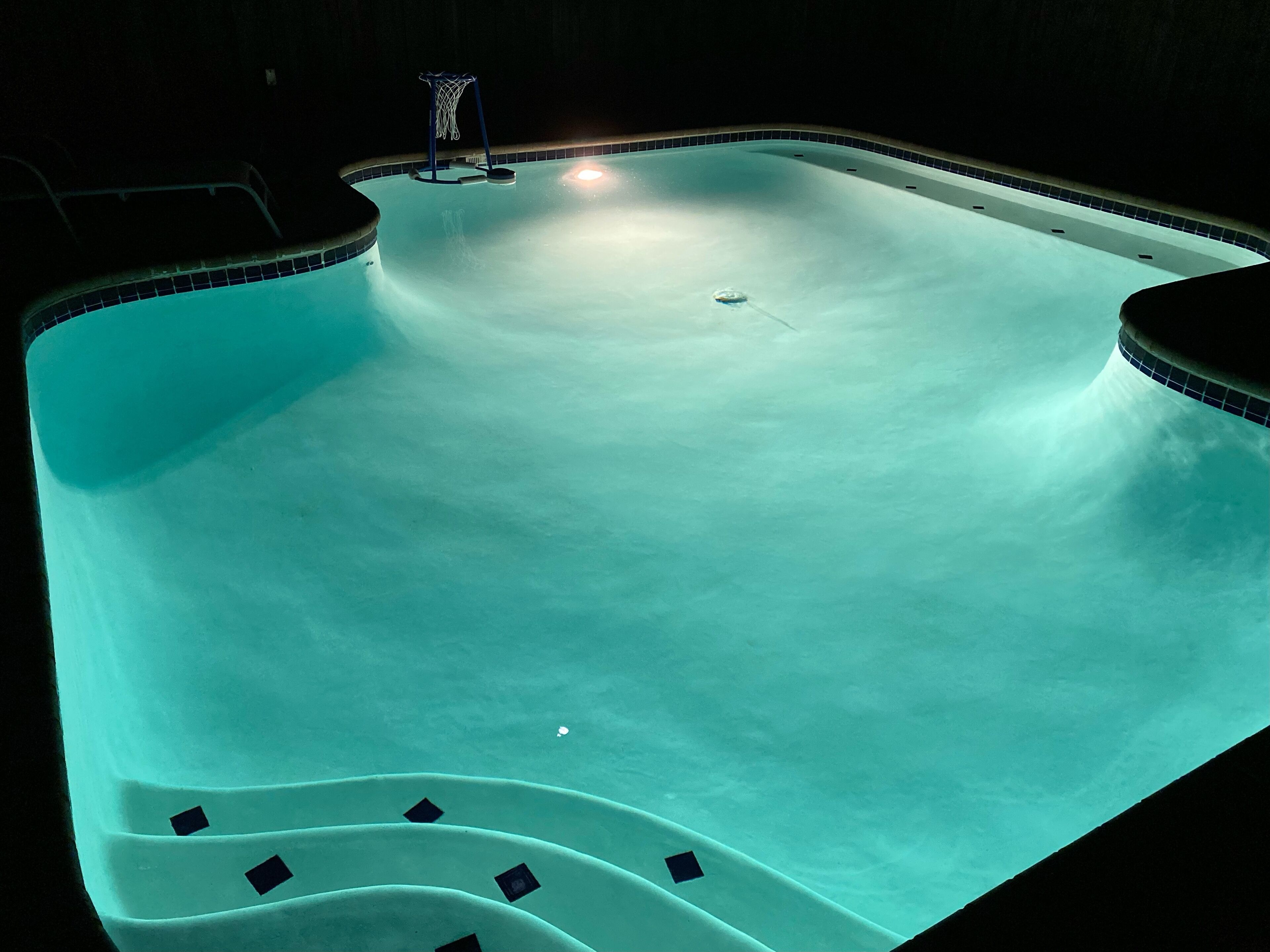 Une piscine avec un panier de basketball et un bord carrelé.