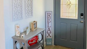 A front door with a frosted glass window, a decorative sign saying "RELAX", and a small console table with a box labeled "SCARABBLE". - Luxurious home /Pool/GameR/BBQ/kingbed/legacyW/Frisco (plano)