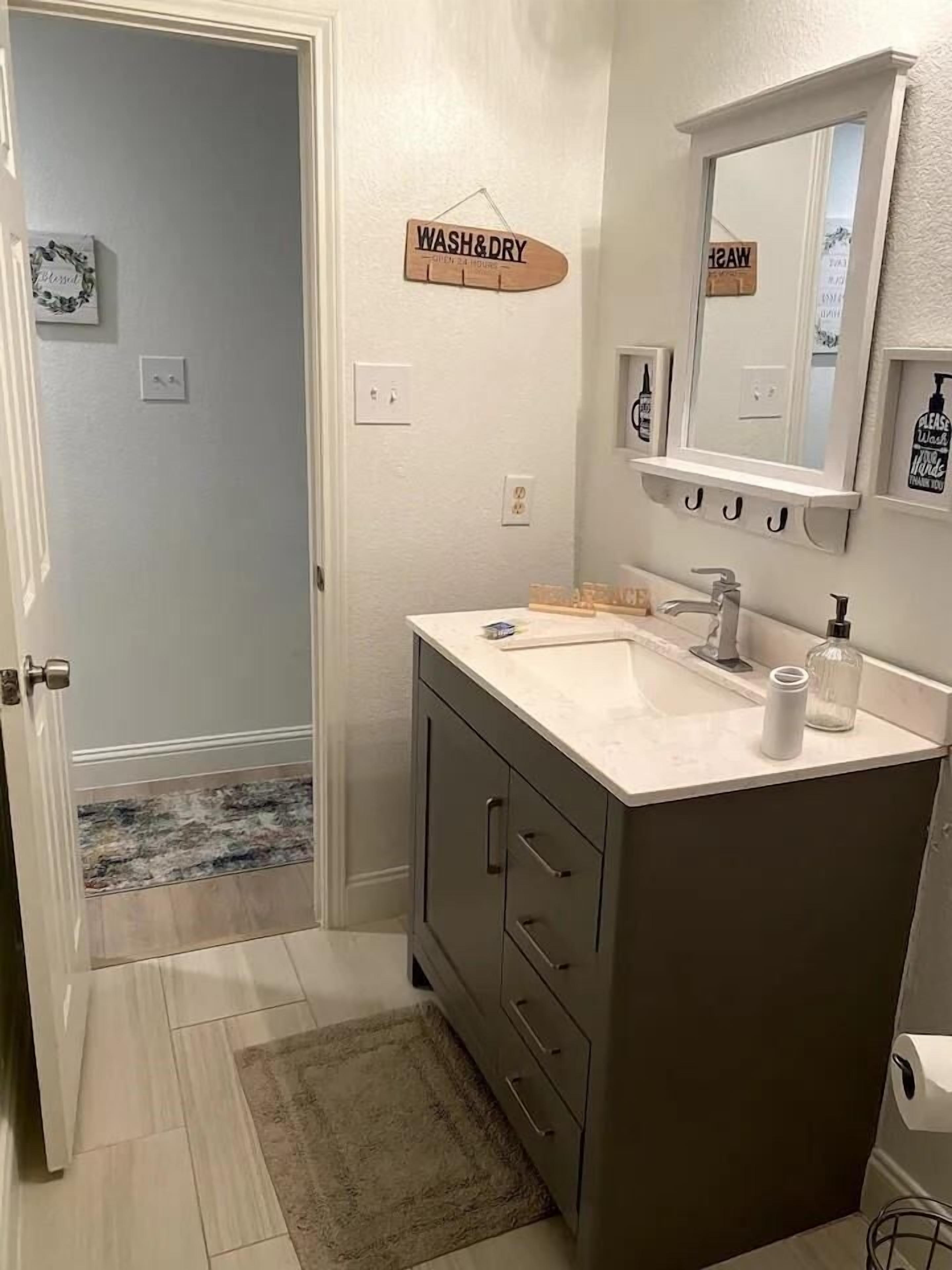 Een badkamer met een wastafel, spiegel en een bord waarop 'WASH & DRY' staat.